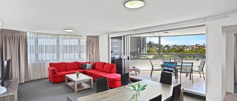 Una habitación de hotel moderna con un sofá rojo, una mesa de comedor y un balcón con vistas a la ciudad.