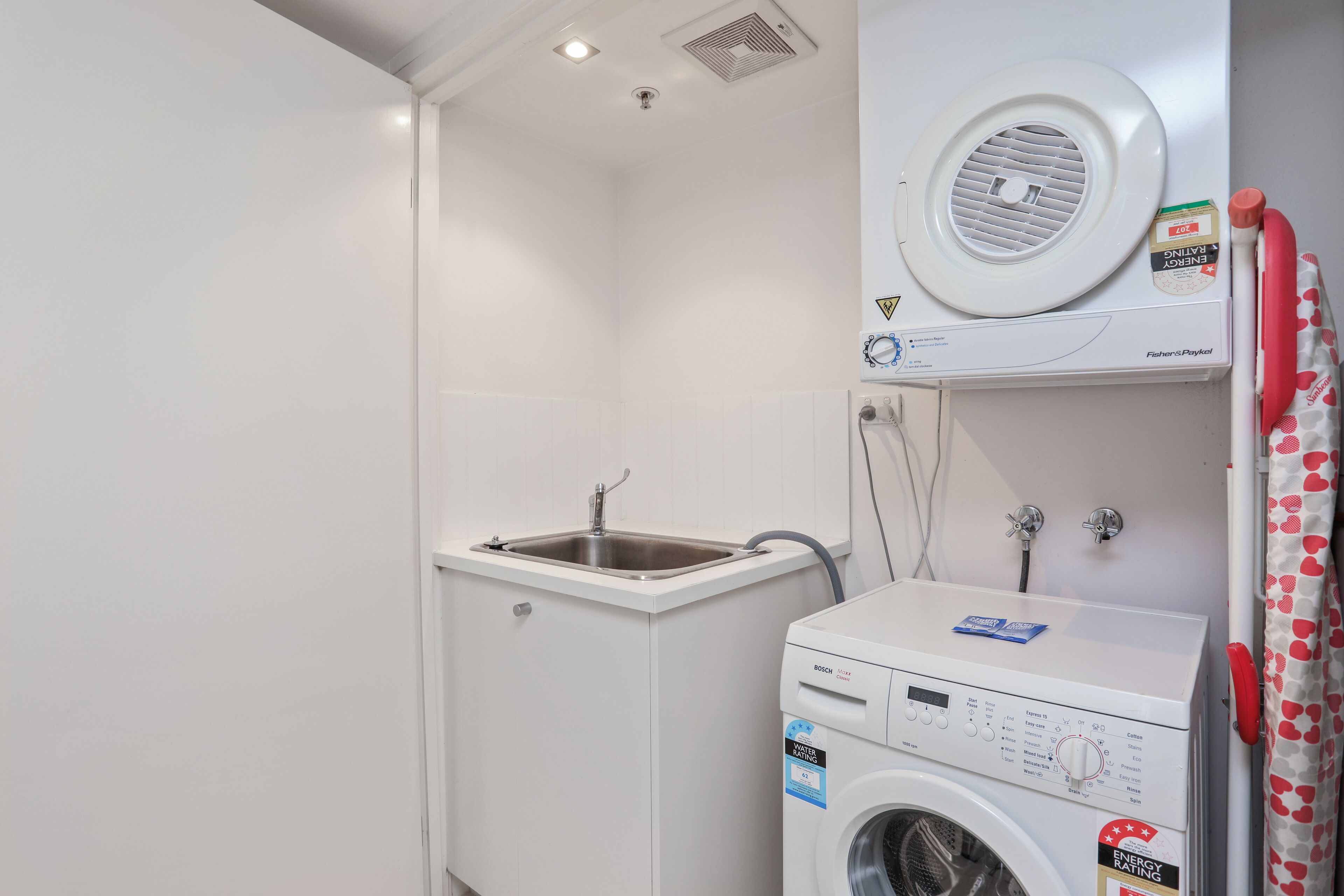 A compact laundry room with a Bosch washing machine, a sink, and a ceiling vent.