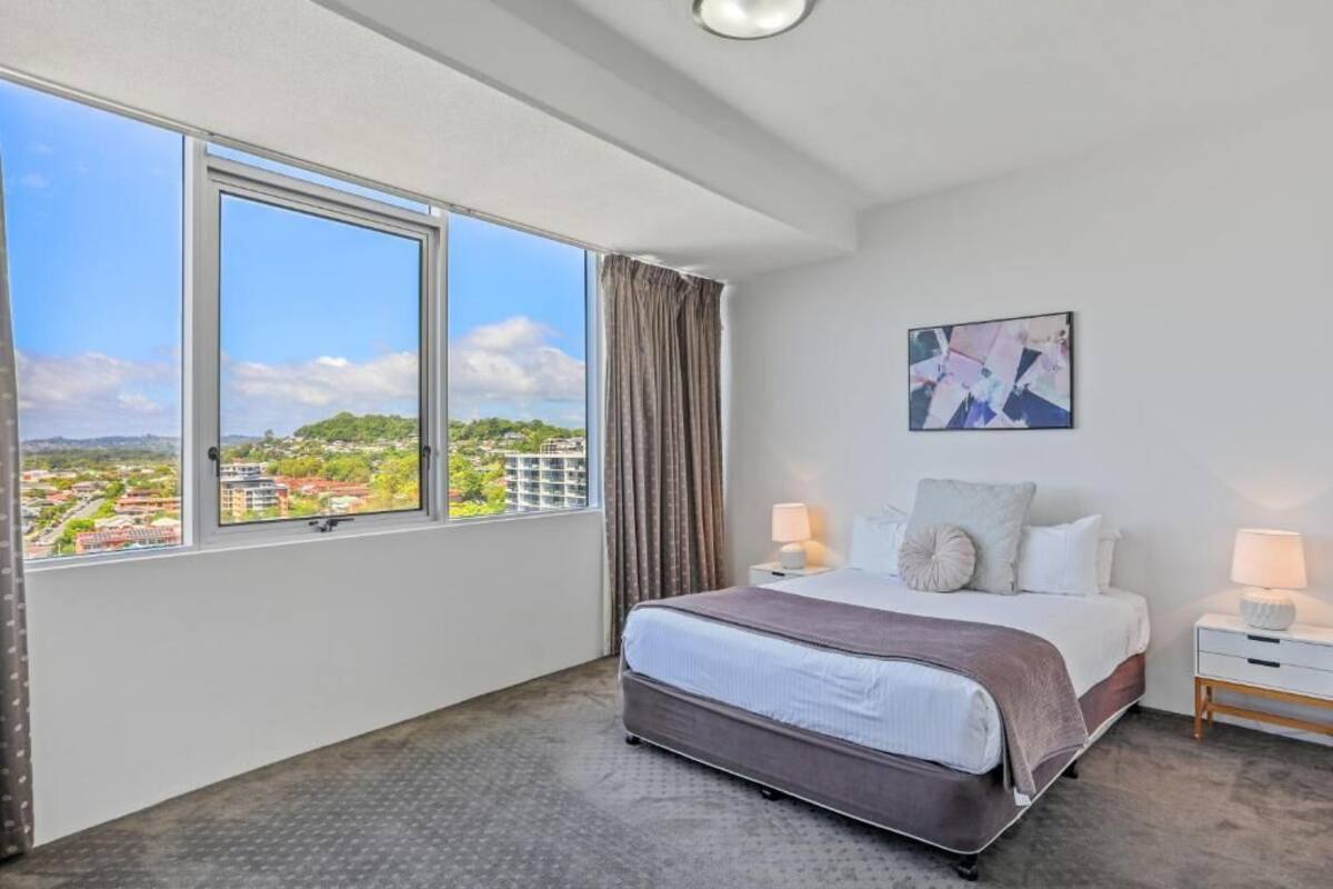 A bedroom with a large window, a bed, a nightstand, and a wall-mounted painting.
