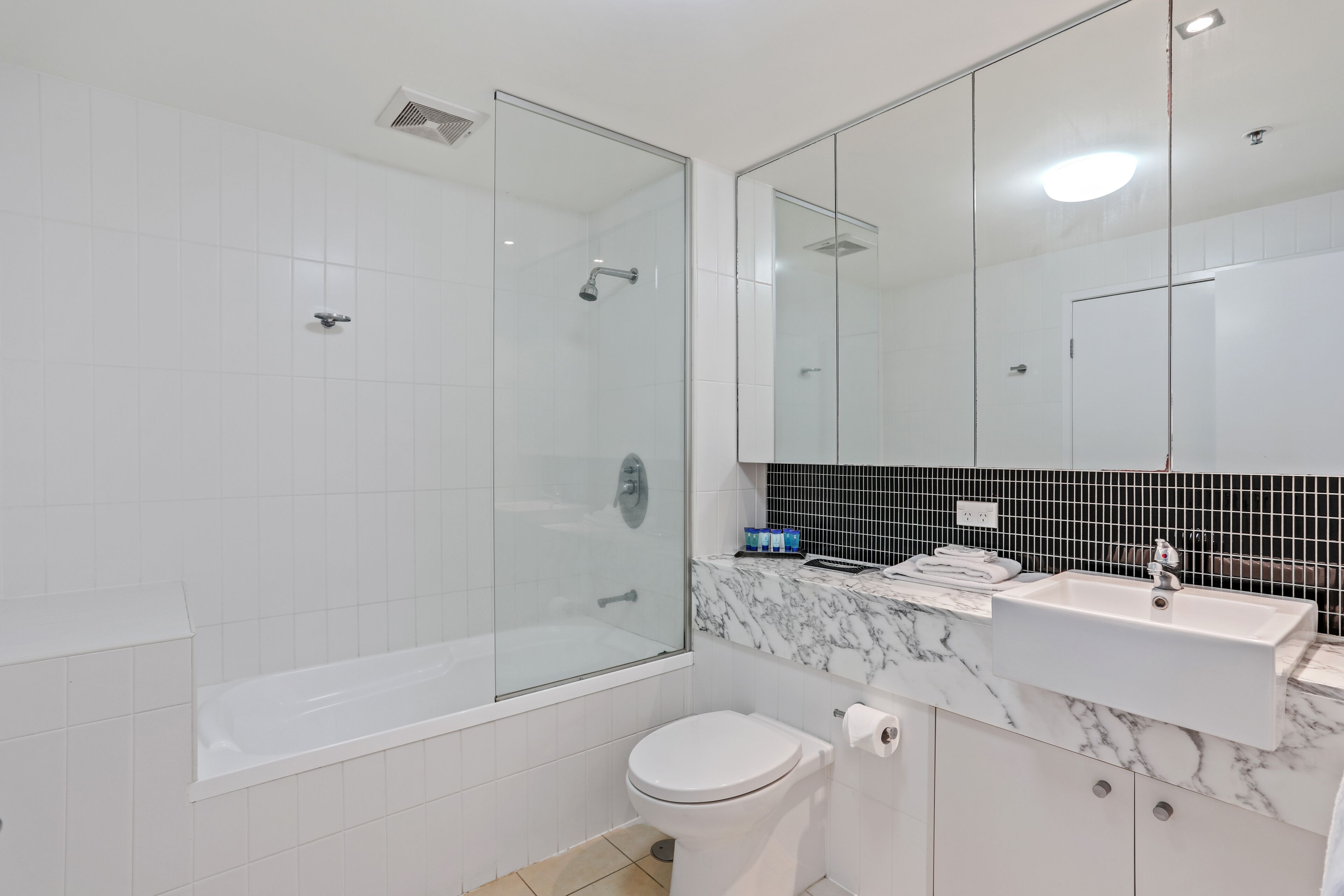 A modern bathroom with a glass-enclosed shower, a white toilet, and a marble sink.
