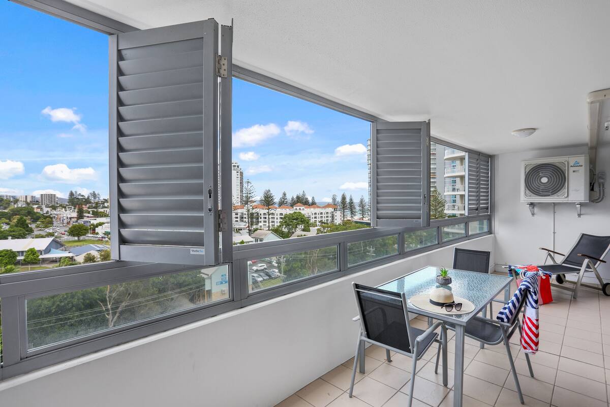 A balcony with a table, chairs, and a view of a cityscape.