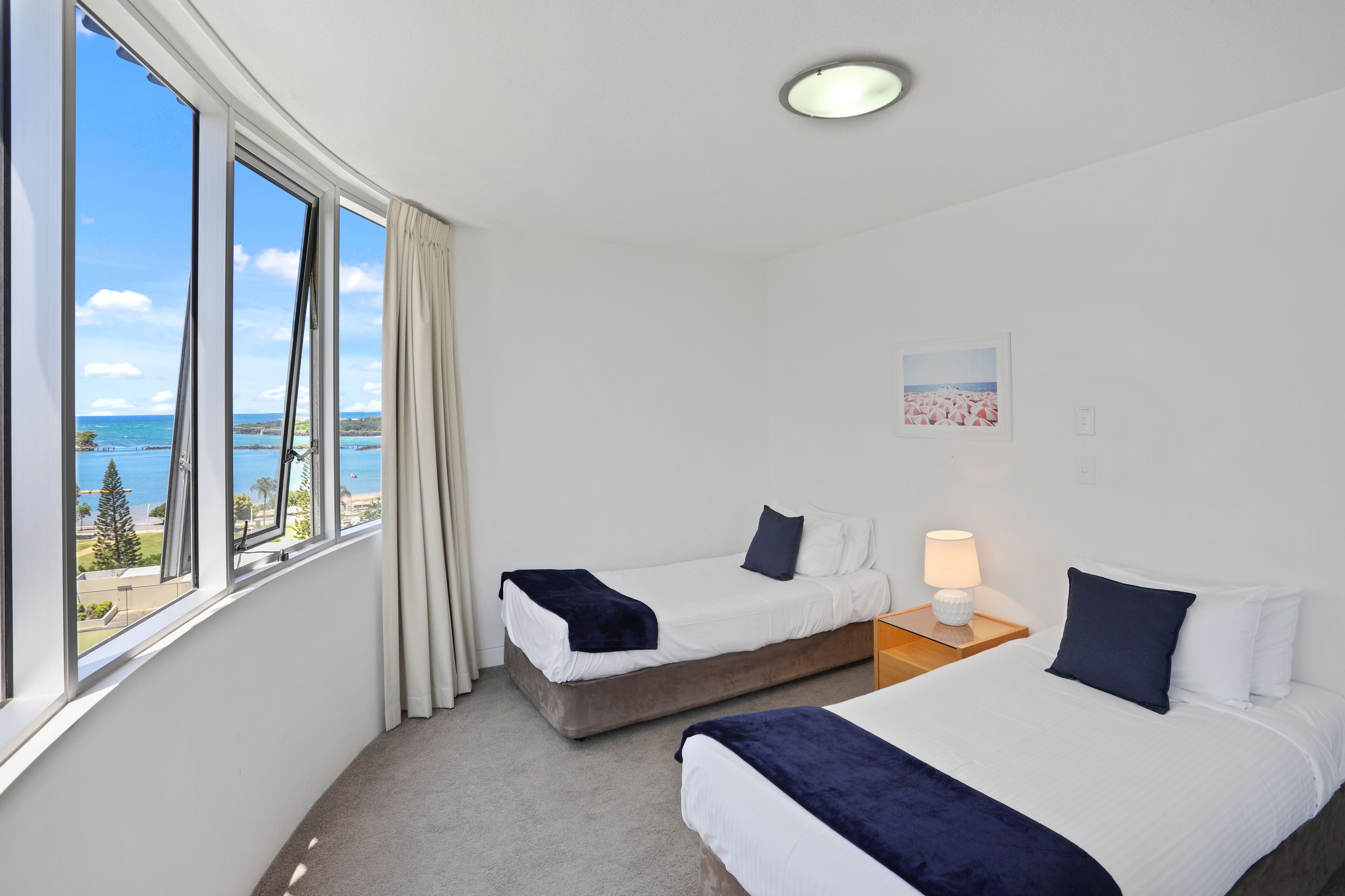 Habitación de hotel con dos camas, vista al mar y una lámpara en el techo.
