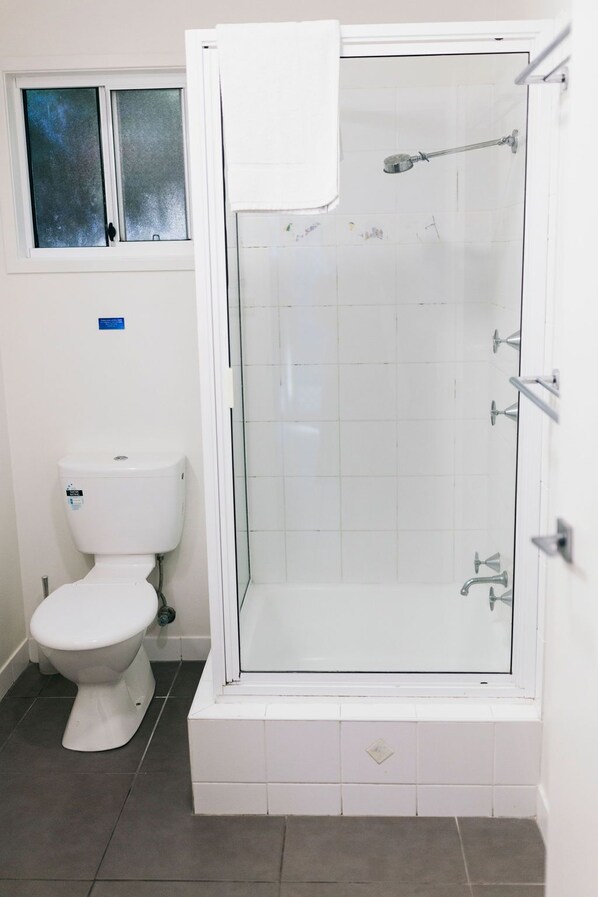 Un baño con ducha de vidrio, inodoro y ventana.