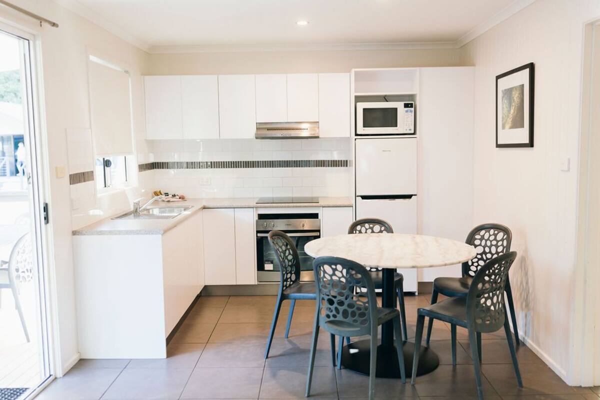 A modern kitchen with white cabinets, a microwave, and a stove. There is a dining table with chairs in the center.