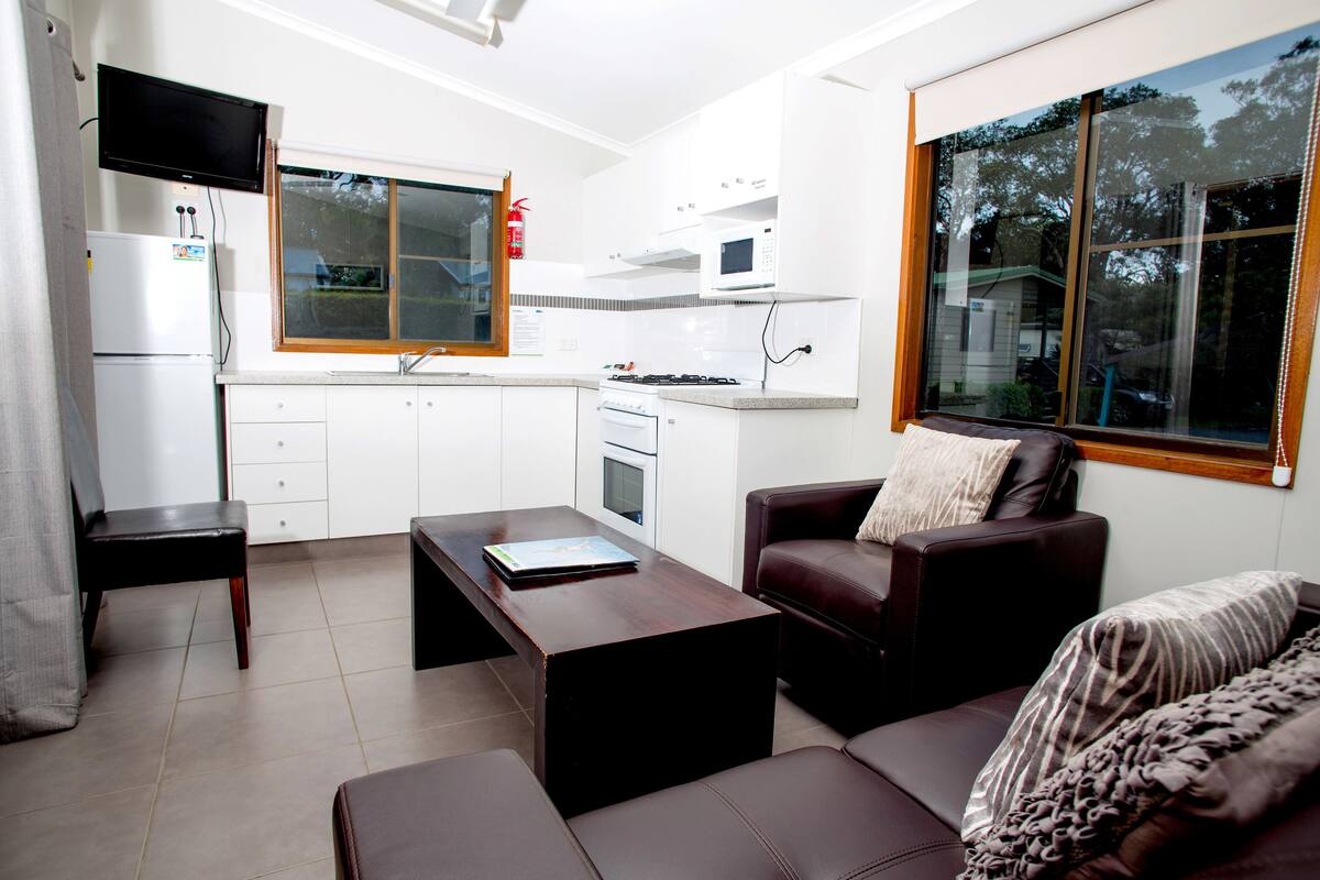 A compact living space with a kitchenette, a sofa, a coffee table, and a TV mounted on the wall.