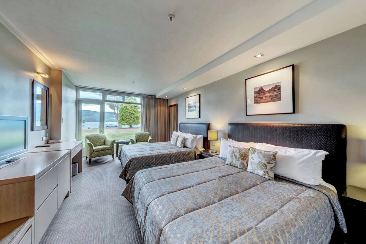 A hotel room with two beds, a desk, a chair, and a large window offering a view of the outdoors.