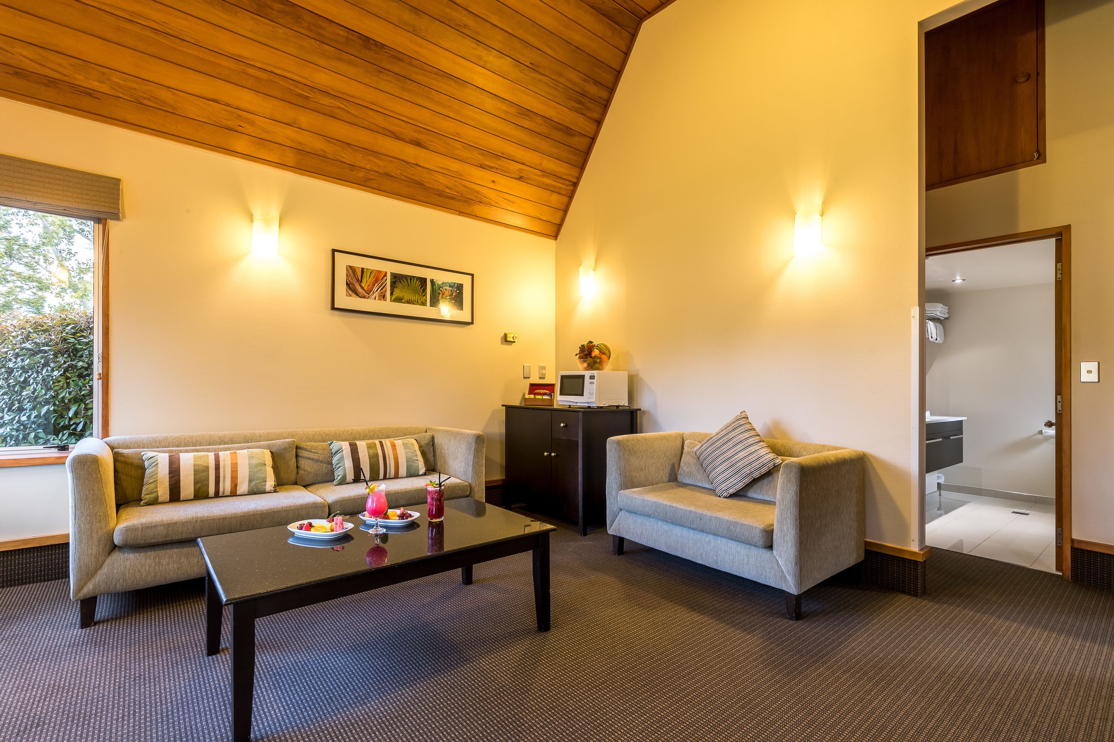 A cozy living room with a sofa, a coffee table, and a cabinet. There is a window providing natural light and a door leading to a bathroom.