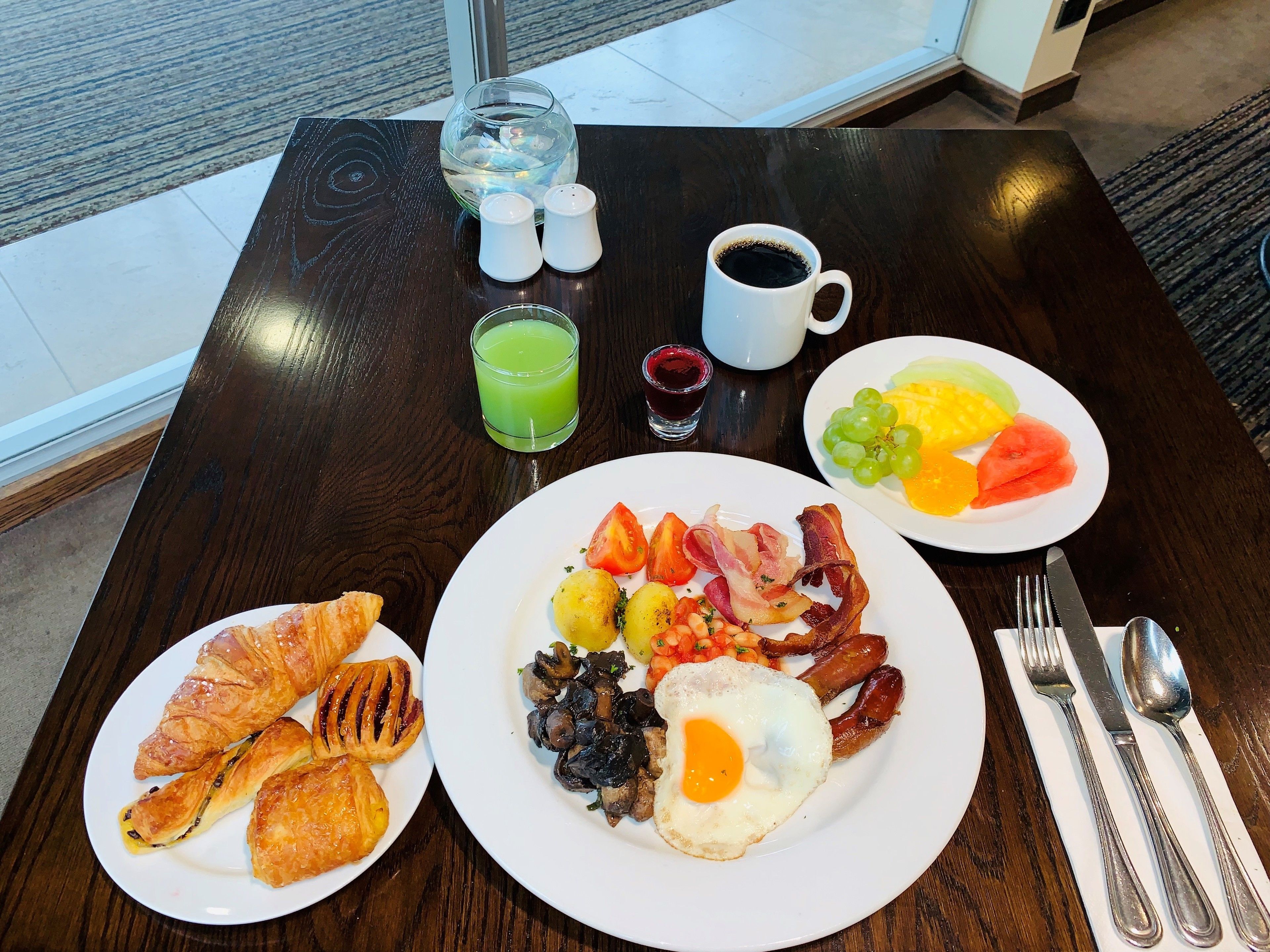 A breakfast table with croissants, eggs, sausages, and a fruit plate.