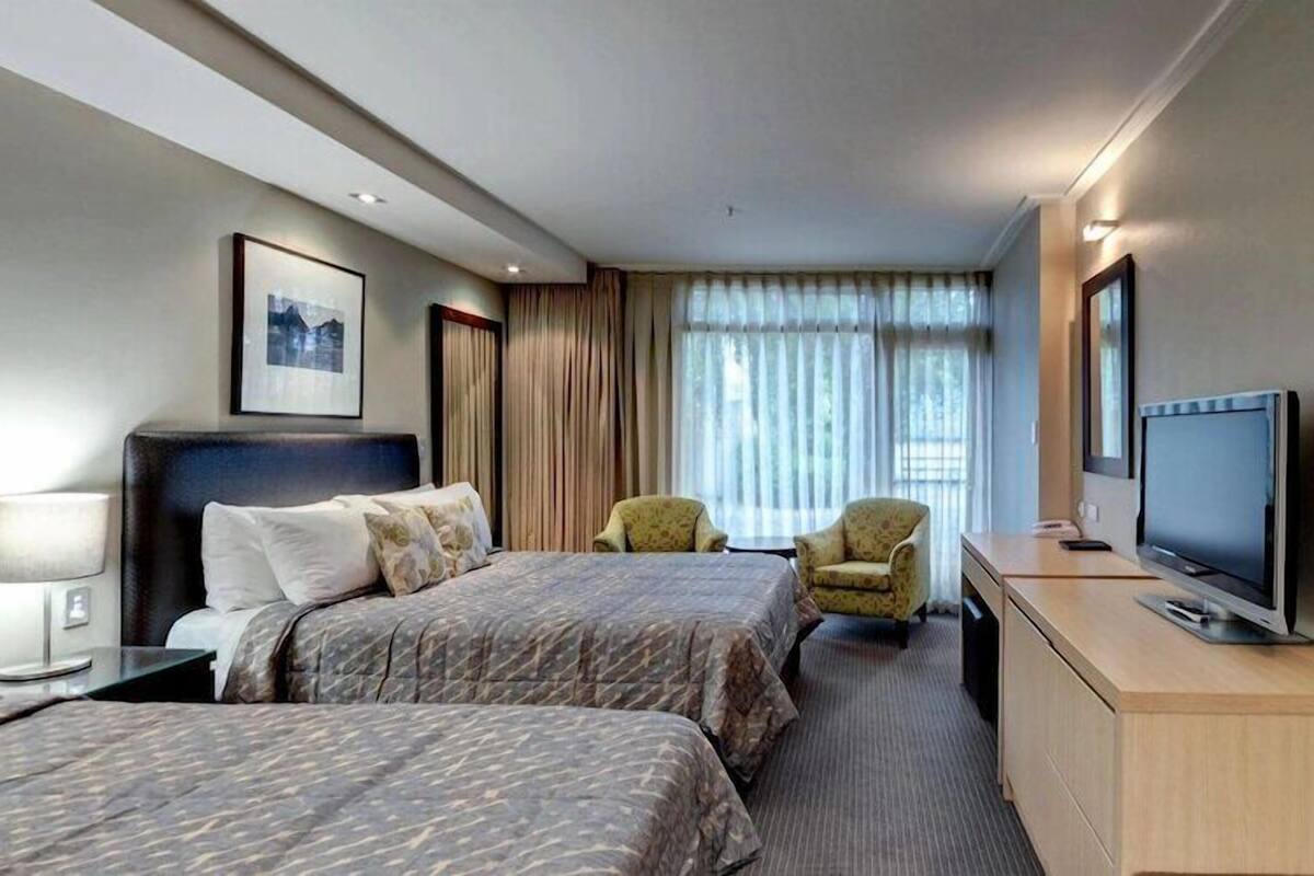 A hotel room with two beds, a desk with a television, a chair, and a window with curtains.