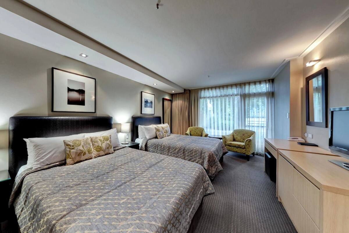 A hotel room with two beds, a desk with a television, a chair, and a nightstand with a lamp.