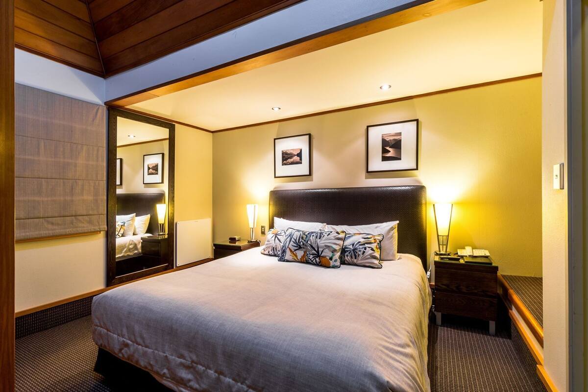 A hotel room with a large bed, bedside lamps, a mirror, and framed pictures on the wall.
