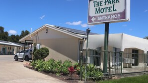 El Motel Park, con un letrero de entrada visible, una zona de estacionamiento y un jardín cercado.