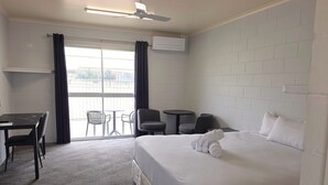 Una habitación de hotel con cama, escritorio, silla, mesita y balcón con vistas.