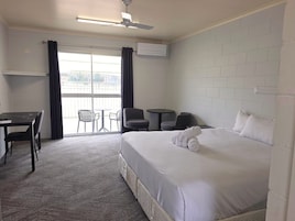 A hotel room with a bed, a desk, a chair, a small table, and a balcony with a view.