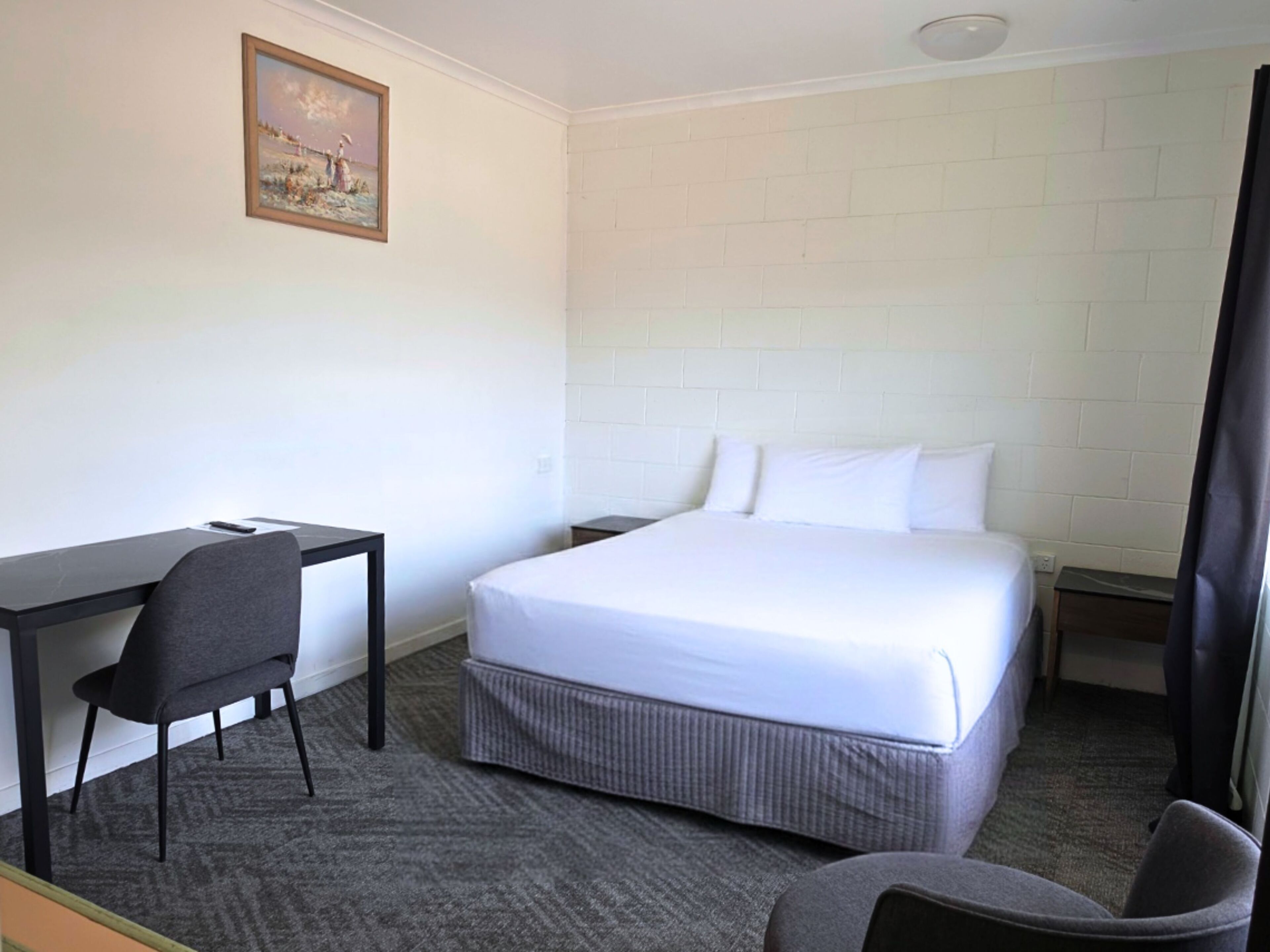 Una camera d'albergo con un letto, una scrivania, una sedia e un quadro appeso al muro.