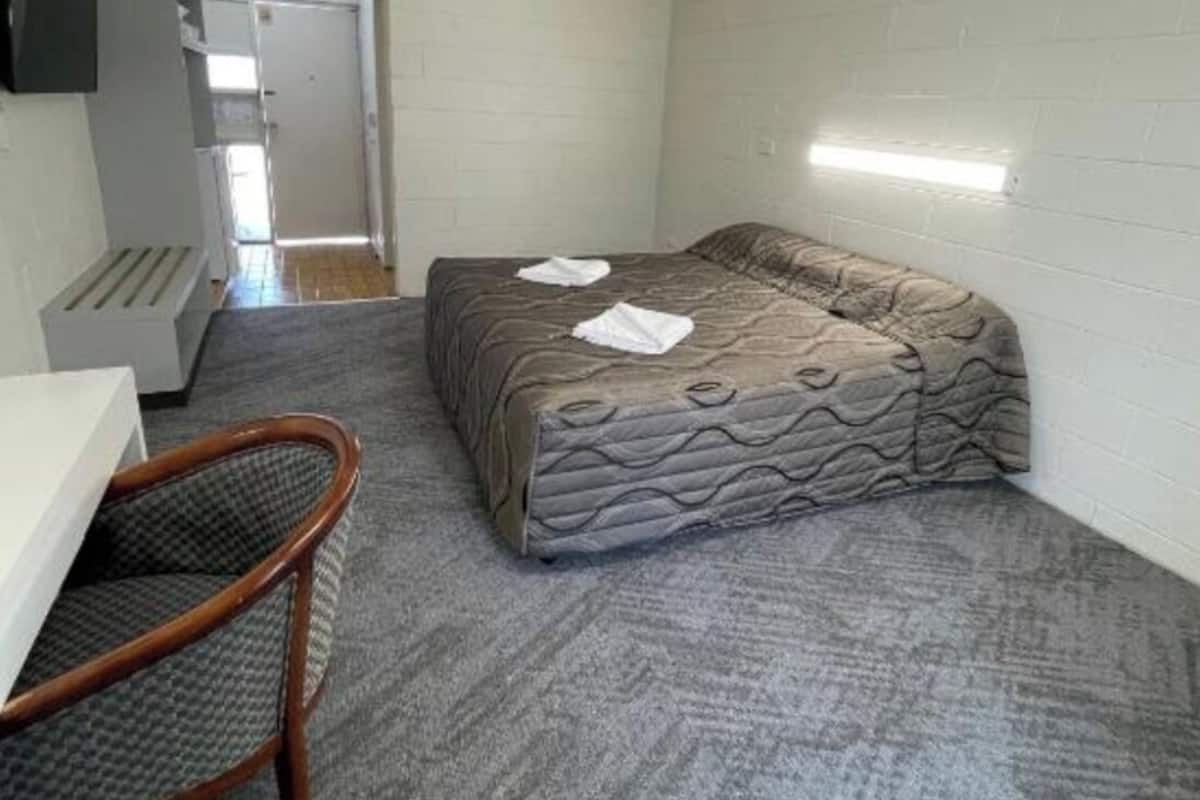 Una habitación pequeña con cama, escritorio, silla, ventilador de techo y televisor.
