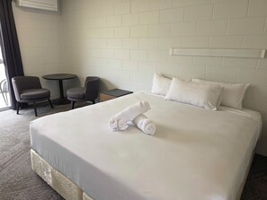 Una habitación de hotel con una cama grande, dos sillas, una mesita pequeña y un aire acondicionado instalado en la pared.