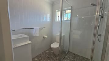 A bathroom with white tiled walls, a glass-enclosed shower, a toilet, and a sink with a towel hanging on the wall.