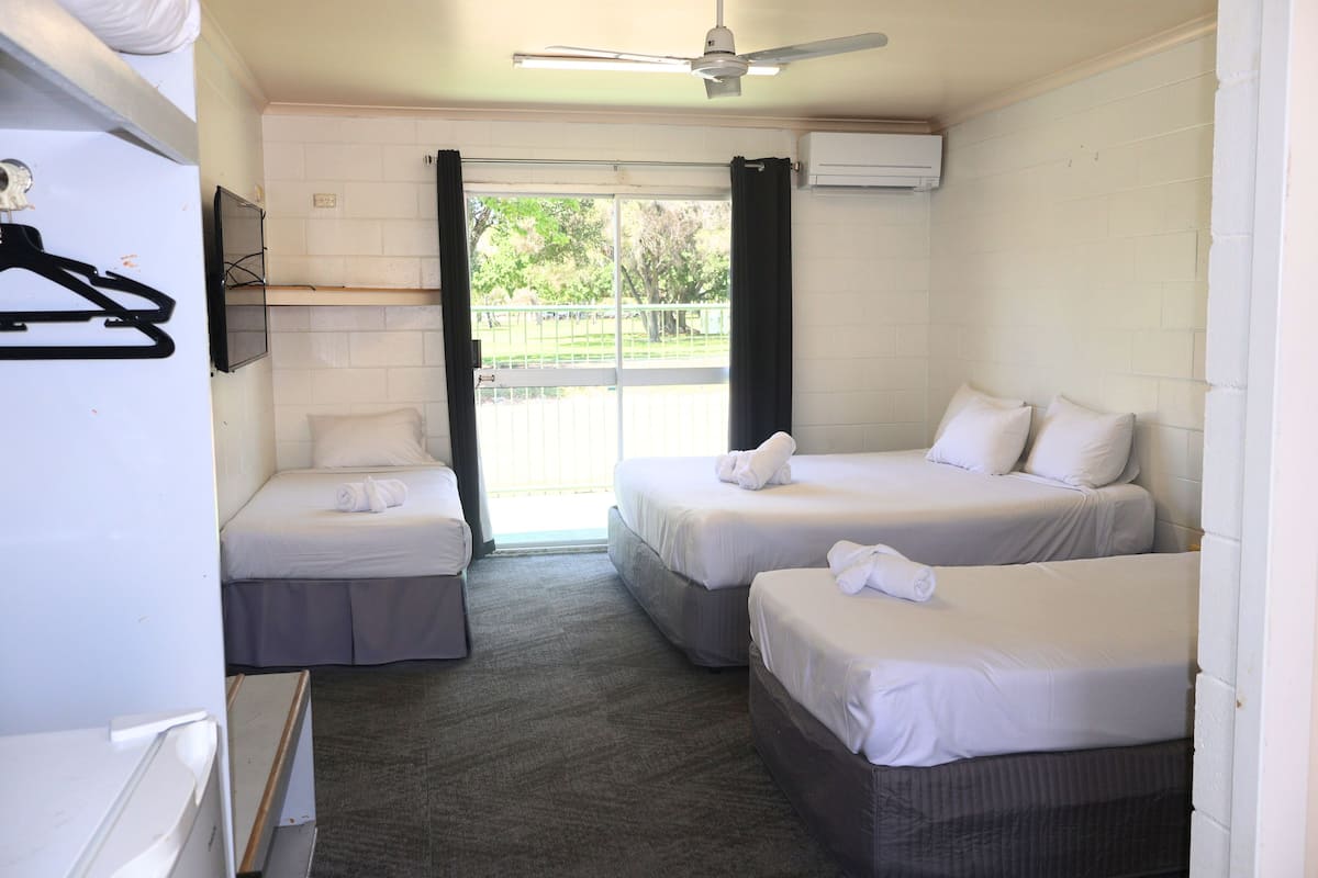 Una habitación de hotel con dos camas, ventilador de techo, aire acondicionado y vistas a través de un ventanal.