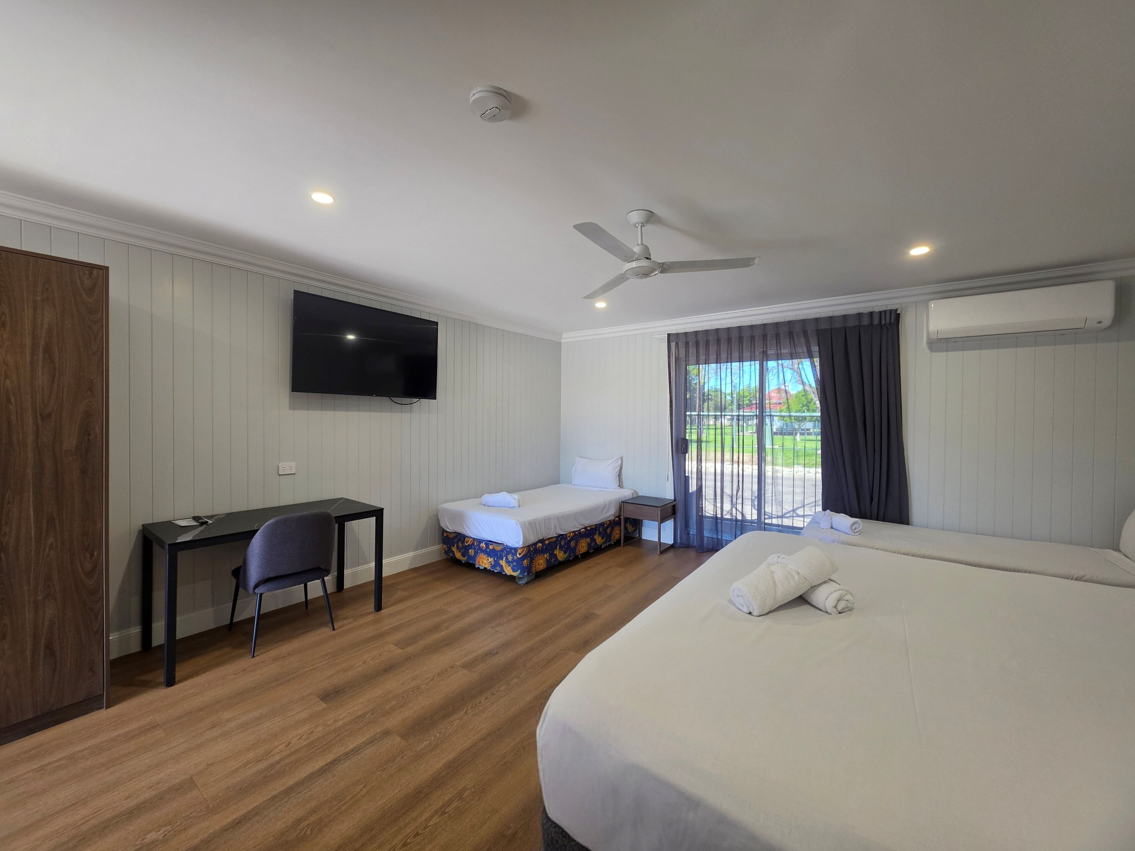Habitación de hotel con cama, escritorio, silla, televisor, ventilador de techo y ventana con cortinas.