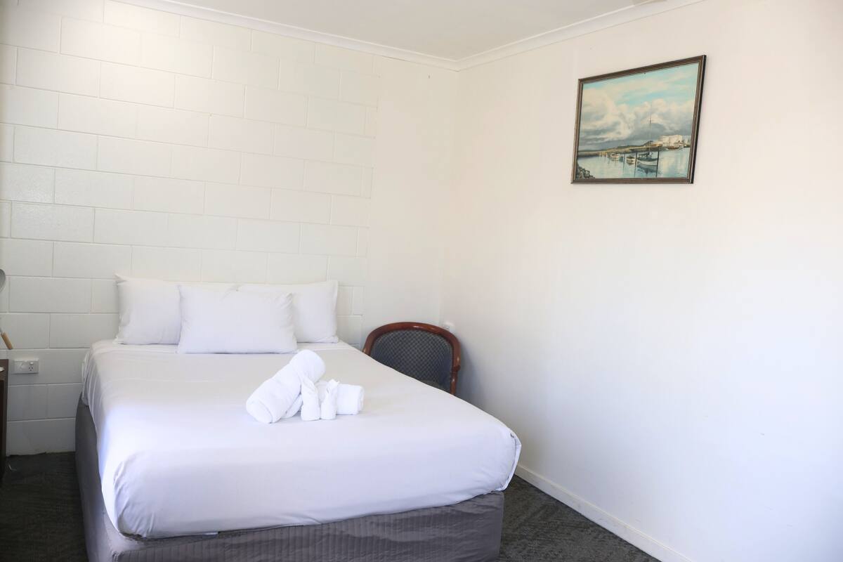 Una habitación de hotel con una cama bien hecha, una silla y un cuadro en la pared.