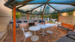 Un patio exterior con un área de estar cubierta, una parrilla y una mesa con sillas.