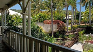 Un espace extérieur abrité doté d’une terrasse en bois, entouré d’une végétation tropicale luxuriante et de palmiers.