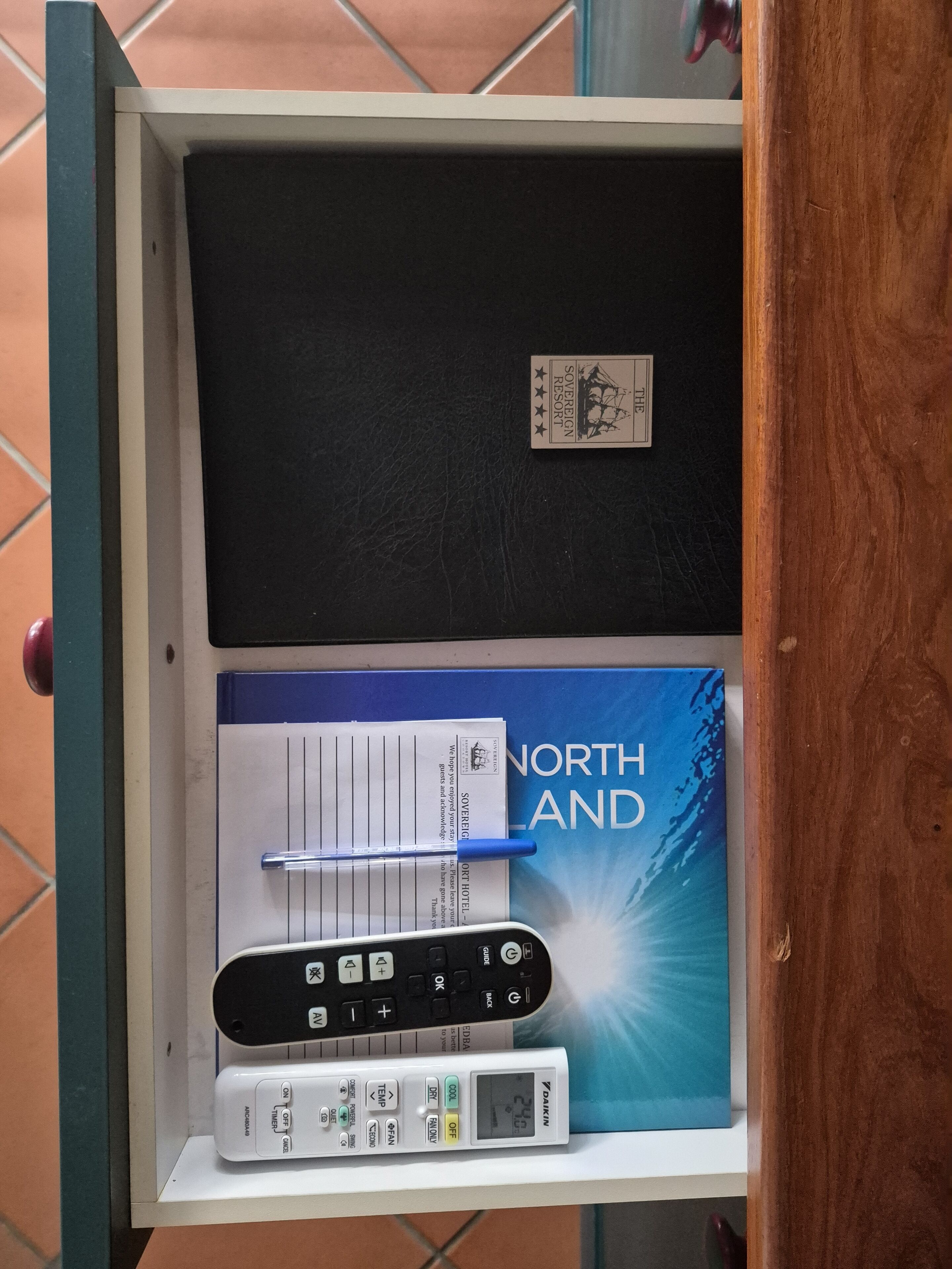 Un tiroir contenant un classeur noir, une brochure de Northland, un stylo et un climatiseur Daikin.