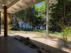 A covered outdoor area with a wooden deck, surrounded by dense greenery and a view of a body of water.