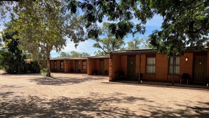 A row of single-story motel buildings with individual rooms, a covered outdoor seating area, and a dirt parking lot. - Territory Manor Motel & Caravan Park (Mataranka)