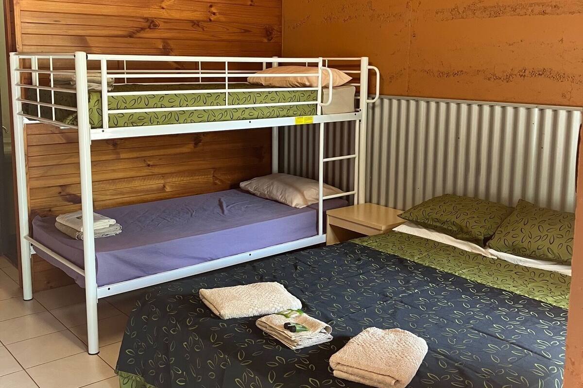 Ein Raum mit Etagenbetten, Holzboden und einer wellenförmigen Wand. Es gibt zwei Betten, eines mit einer violetten Matratze und das andere mit einem grün gemusterten Bettbezug.