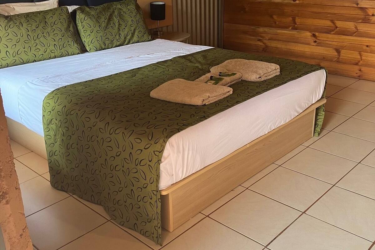 Ein ordentlich bezogenes Bett mit grün gemusterten Betttextilien und zwei Handtüchern auf dem Bett.