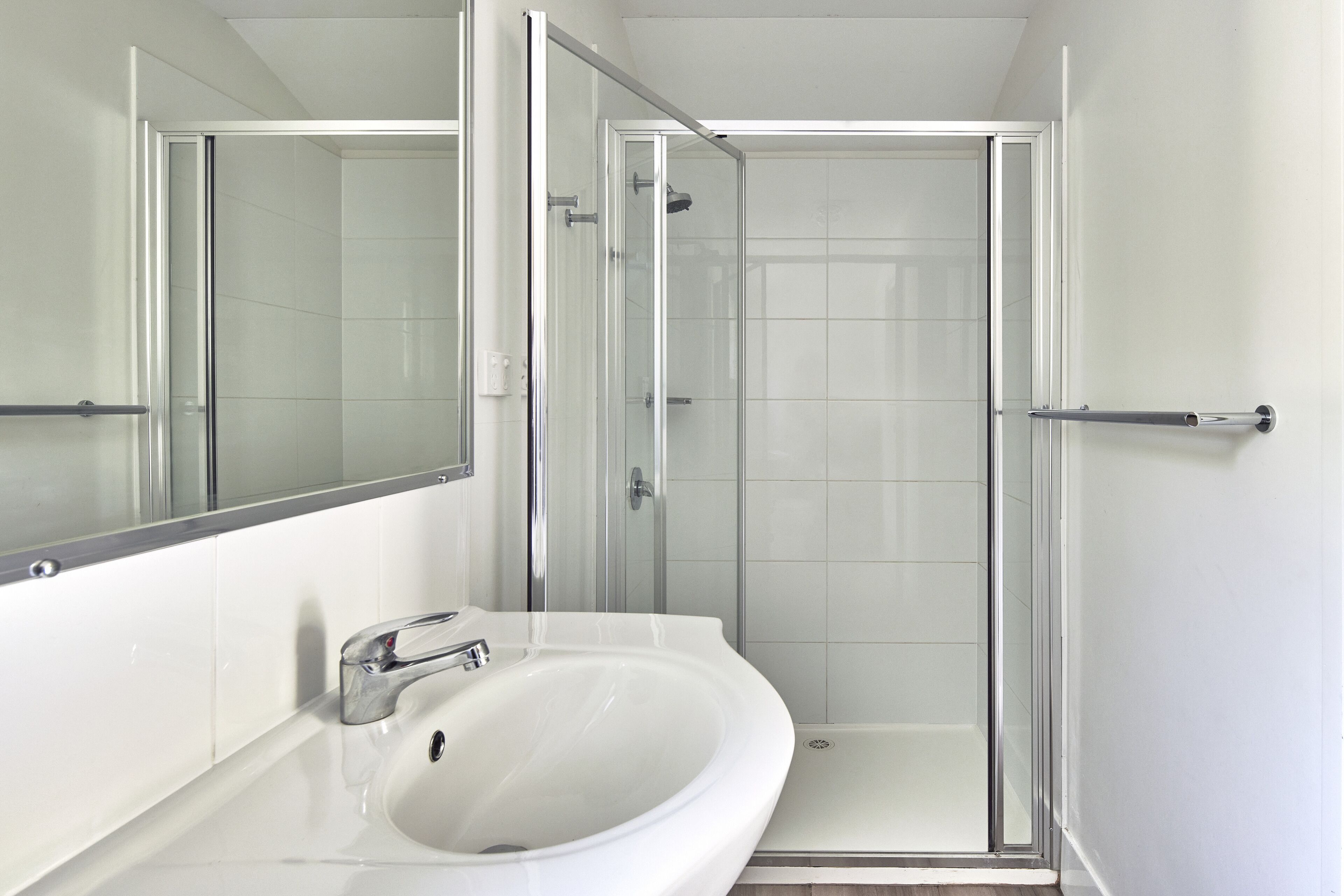 A modern bathroom with a glass-enclosed shower, a white sink, and a large mirror.