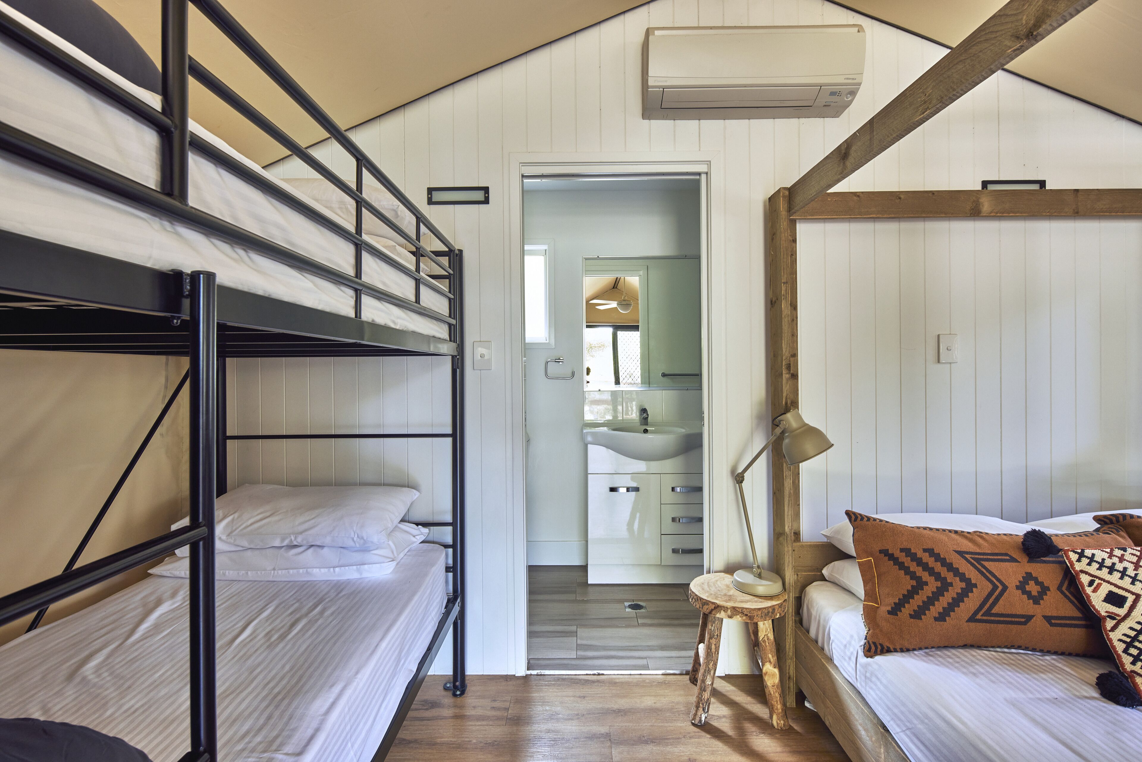 A dormitory room with bunk beds, a small table with a lamp, and a bathroom visible through an open door.