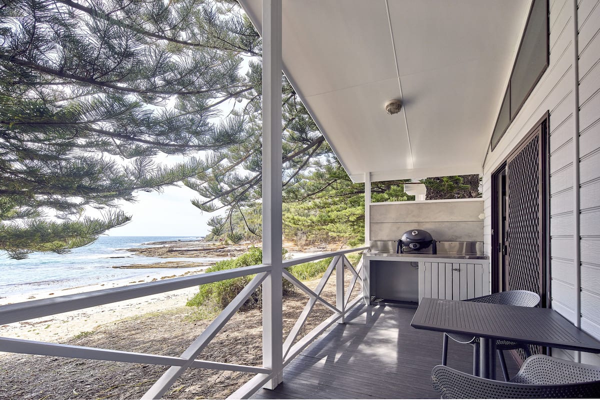 A covered outdoor area with a view of the beach, a grill, and a table with chairs.