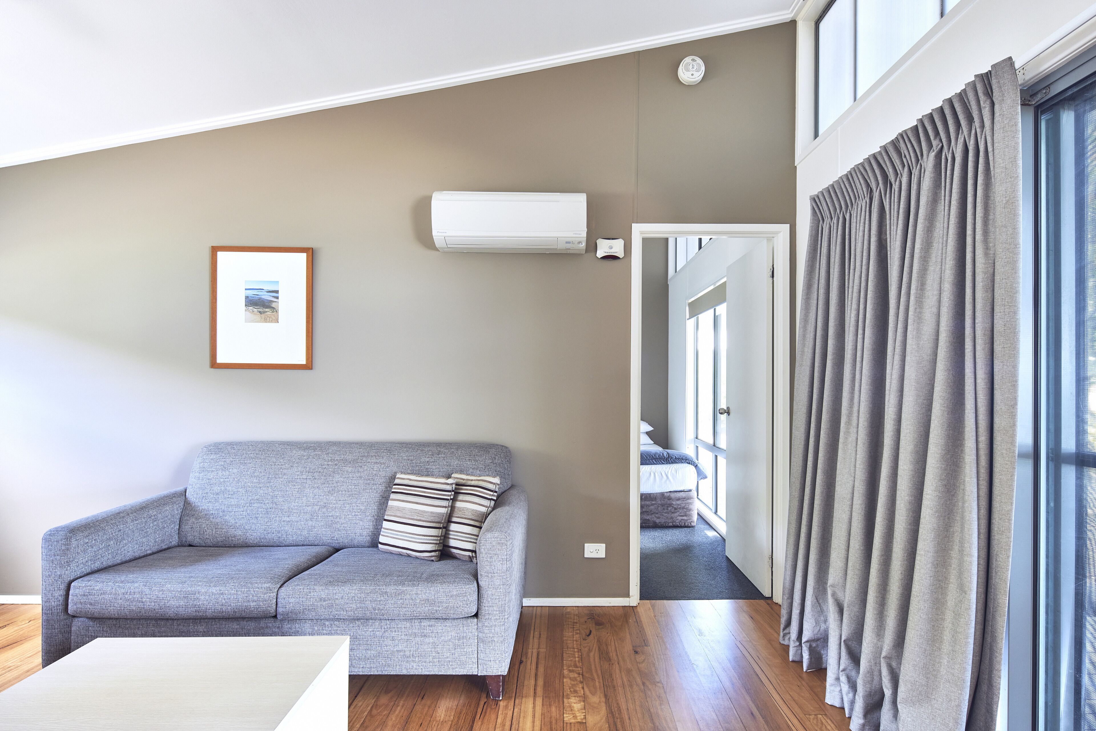 Uma sala de estar moderna com um sofá cinzento, um quadro na parede e uma janela com cortinas cinzas.