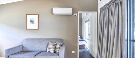 Uma sala de estar moderna com um sofá cinzento, um quadro na parede e uma janela com cortinas cinzas.