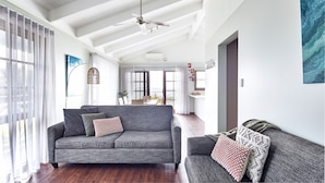 Un vaste espace de vie comprenant un canapé gris, un fauteuil plus petit et un ventilateur de plafond.