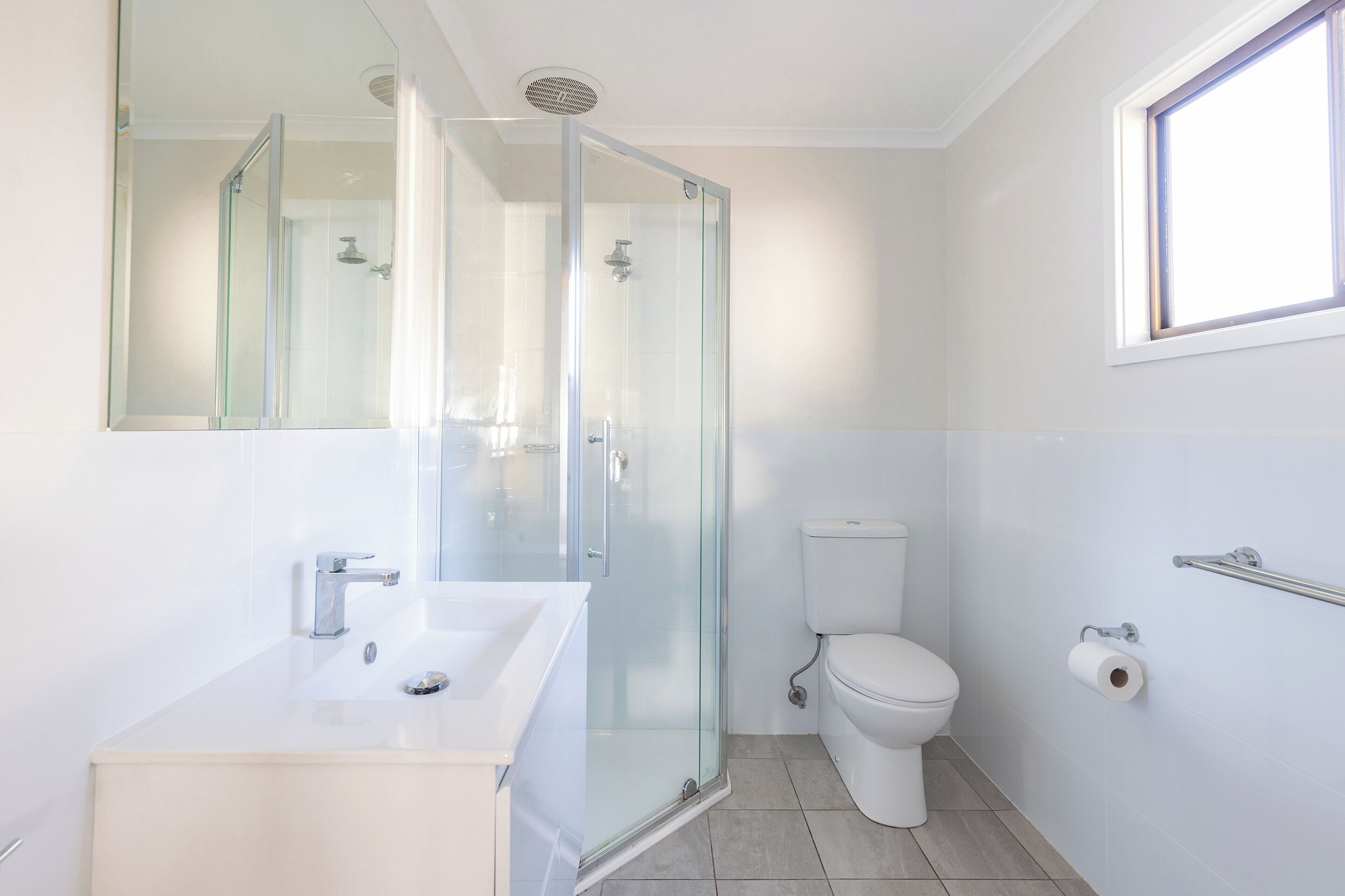Een moderne badkamer met een douchecabine van glas, een wit wastafeltje en een toilet.
