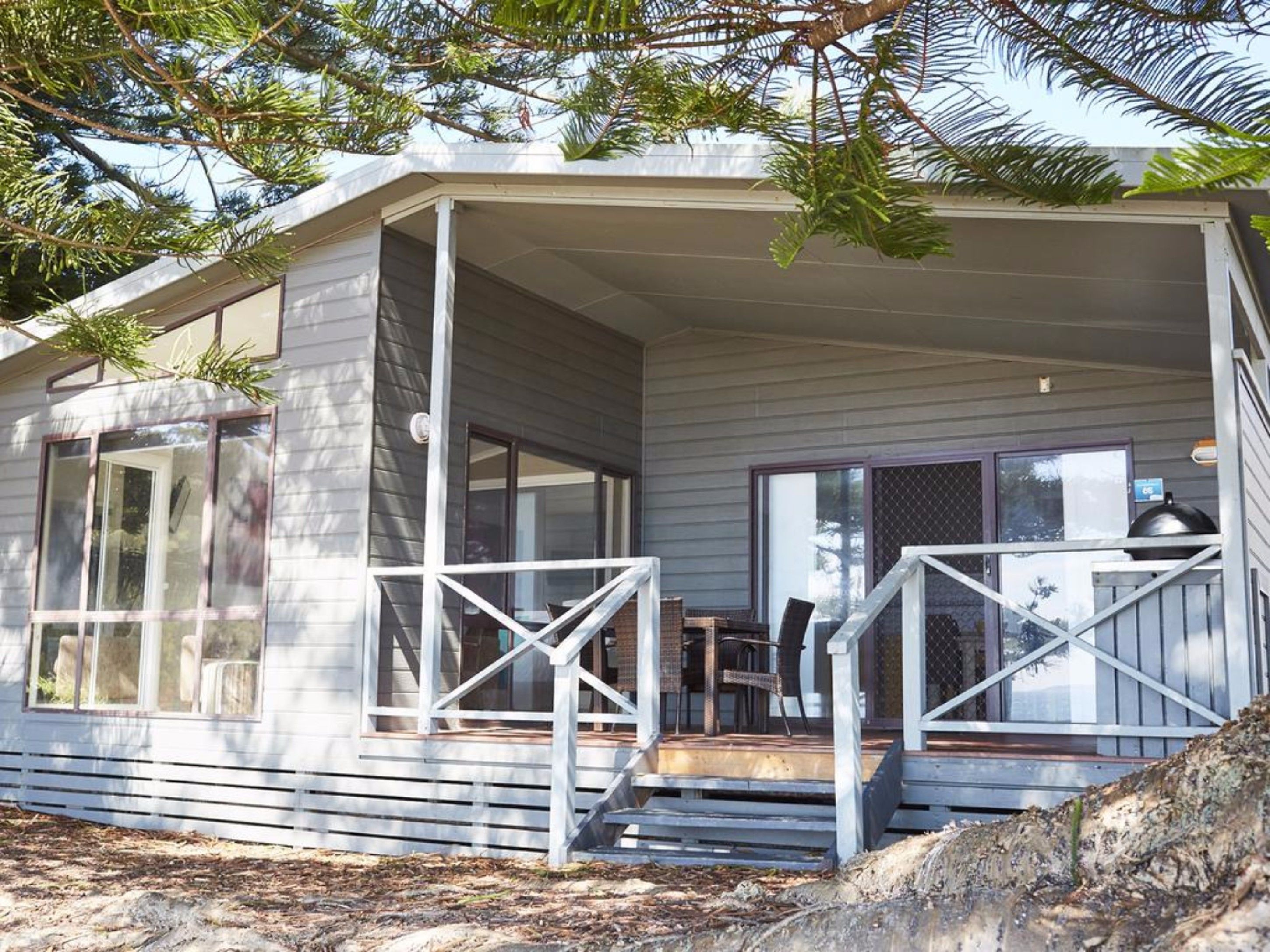 Une maison de plain-pied dotée d’un porche couvert, de grandes fenêtres et d’un barbecue visible.