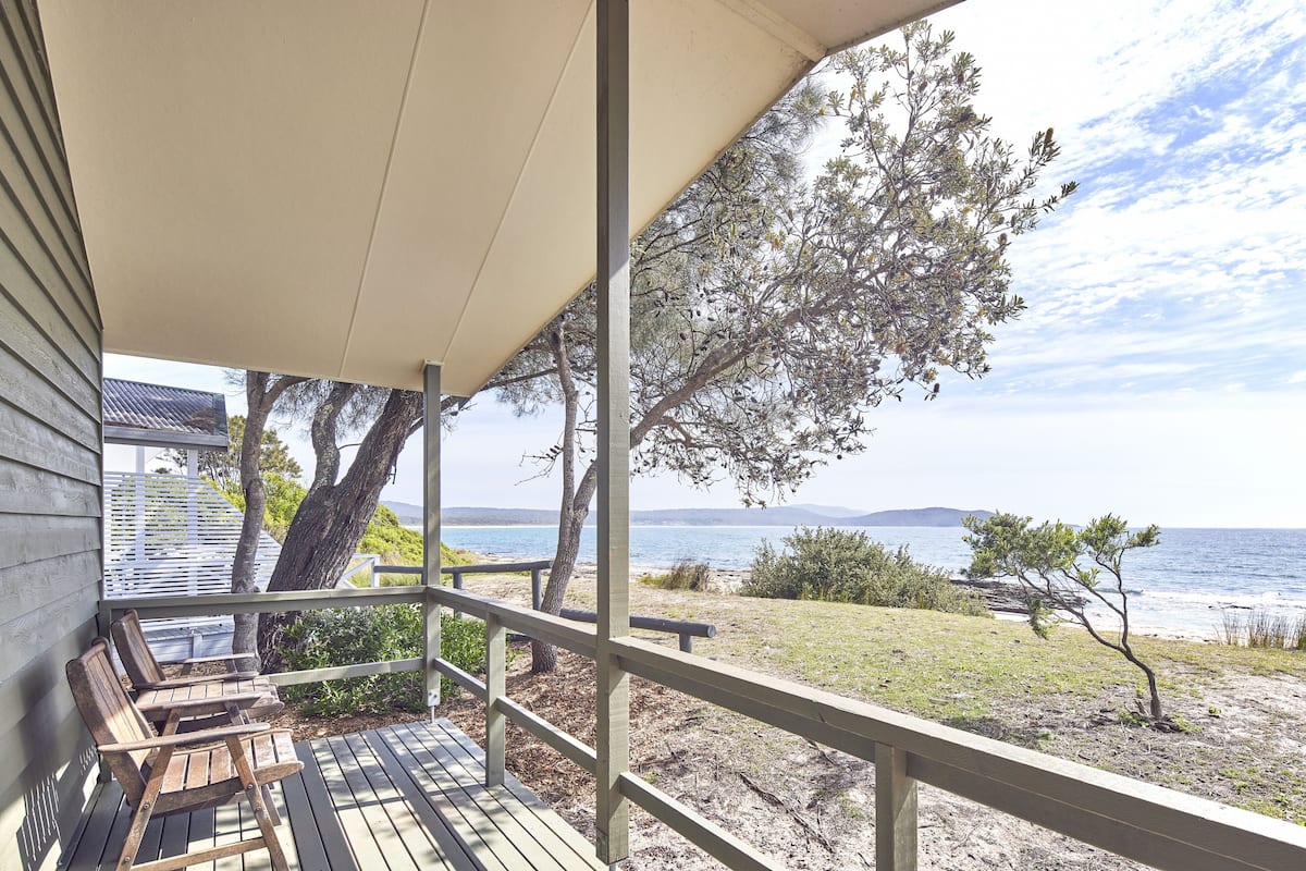 A covered porch with wooden benches, a view of the beach, and a tree.