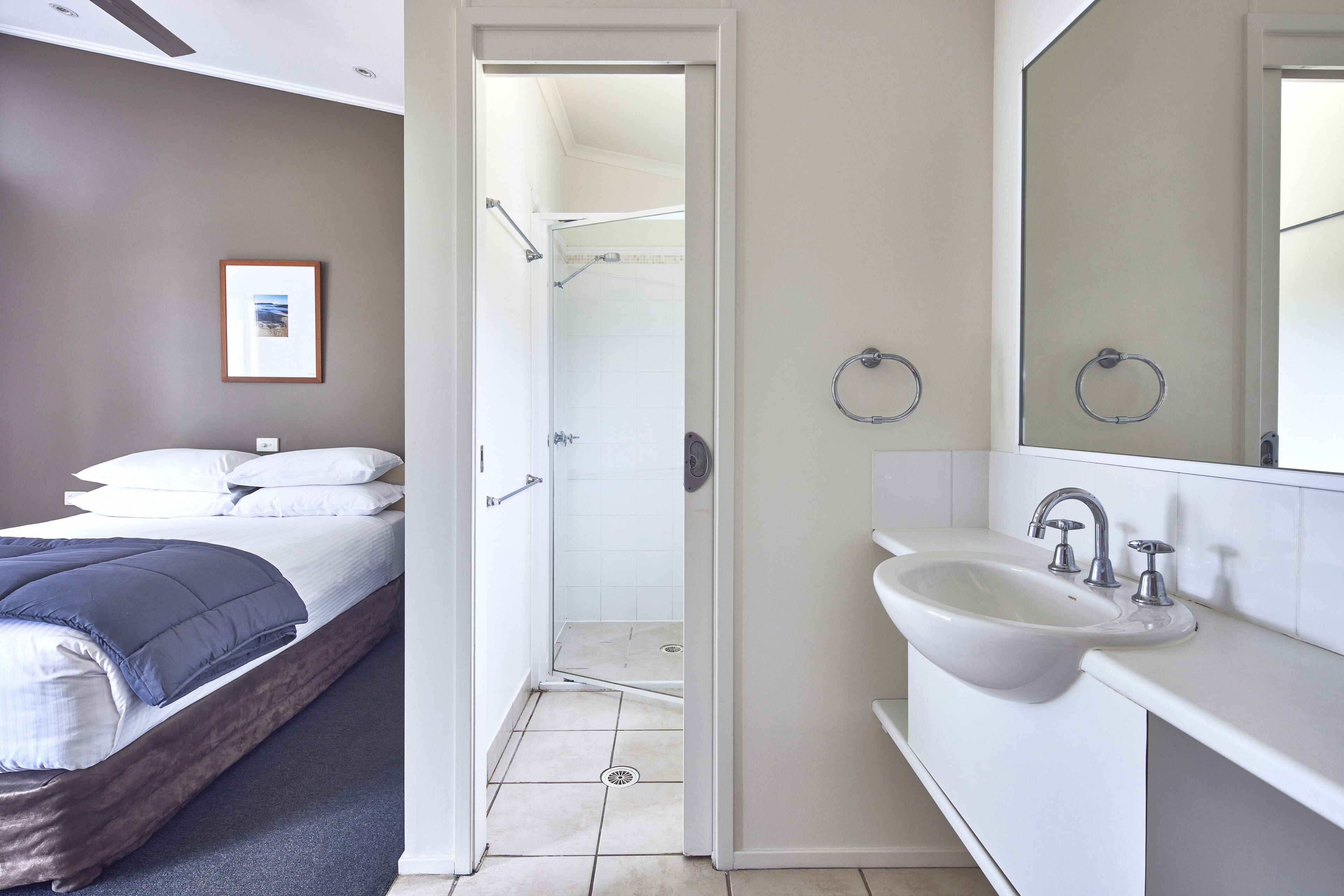 A bedroom with a bed, a bathroom with a sink and mirror, and a shower.