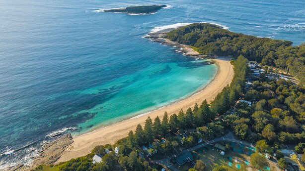 Vue aérienne d’une zone côtière avec une plage, des eaux d’un bleu limpide et une petite île.