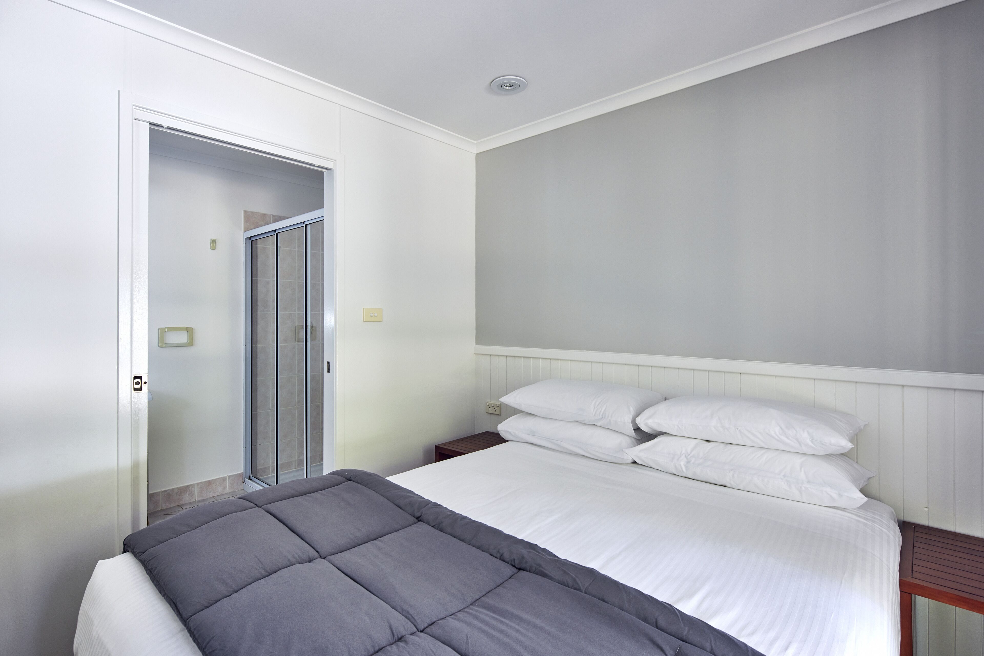 A bedroom with a bed, a nightstand, a wooden headboard, a white door, and a glass shower door.