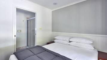 A bedroom with a bed, a nightstand, a wooden headboard, a white door, and a glass shower door.