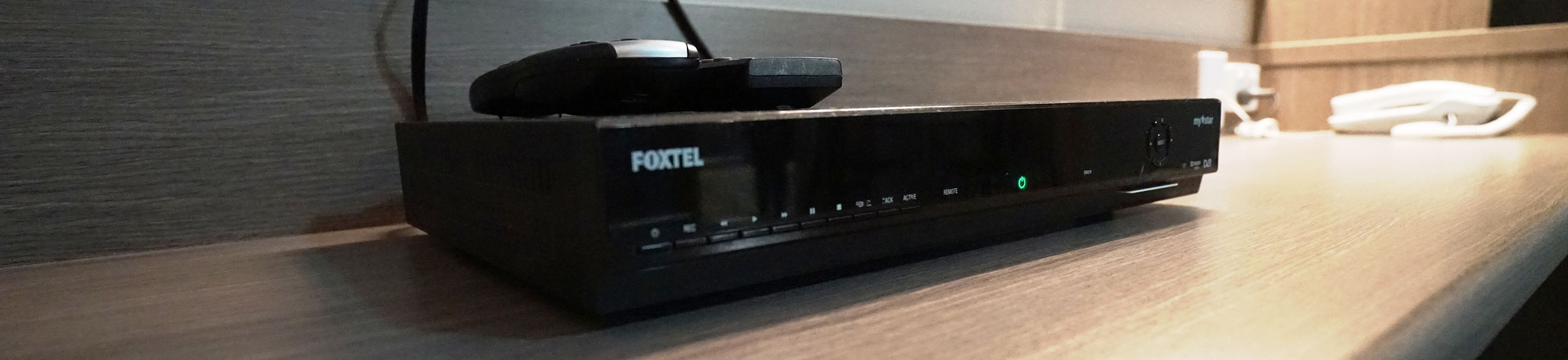 Un appareil Foxtel noir posé sur une surface en bois, avec une télécommande dessus.