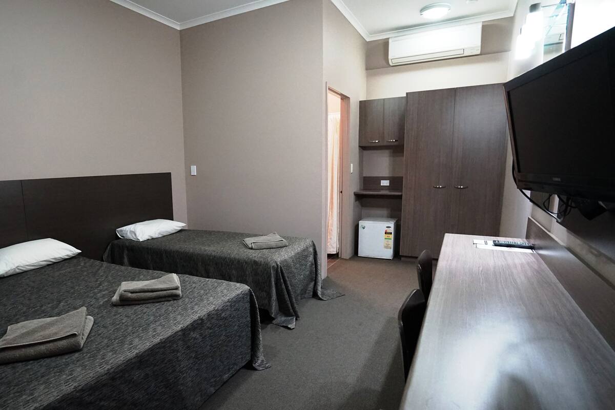 A hotel room with two single beds, a desk, a television, and a mini-fridge.
