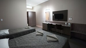 Habitación de hotel con dos camas individuales, un escritorio con silla, televisor montado en la pared y un armario.