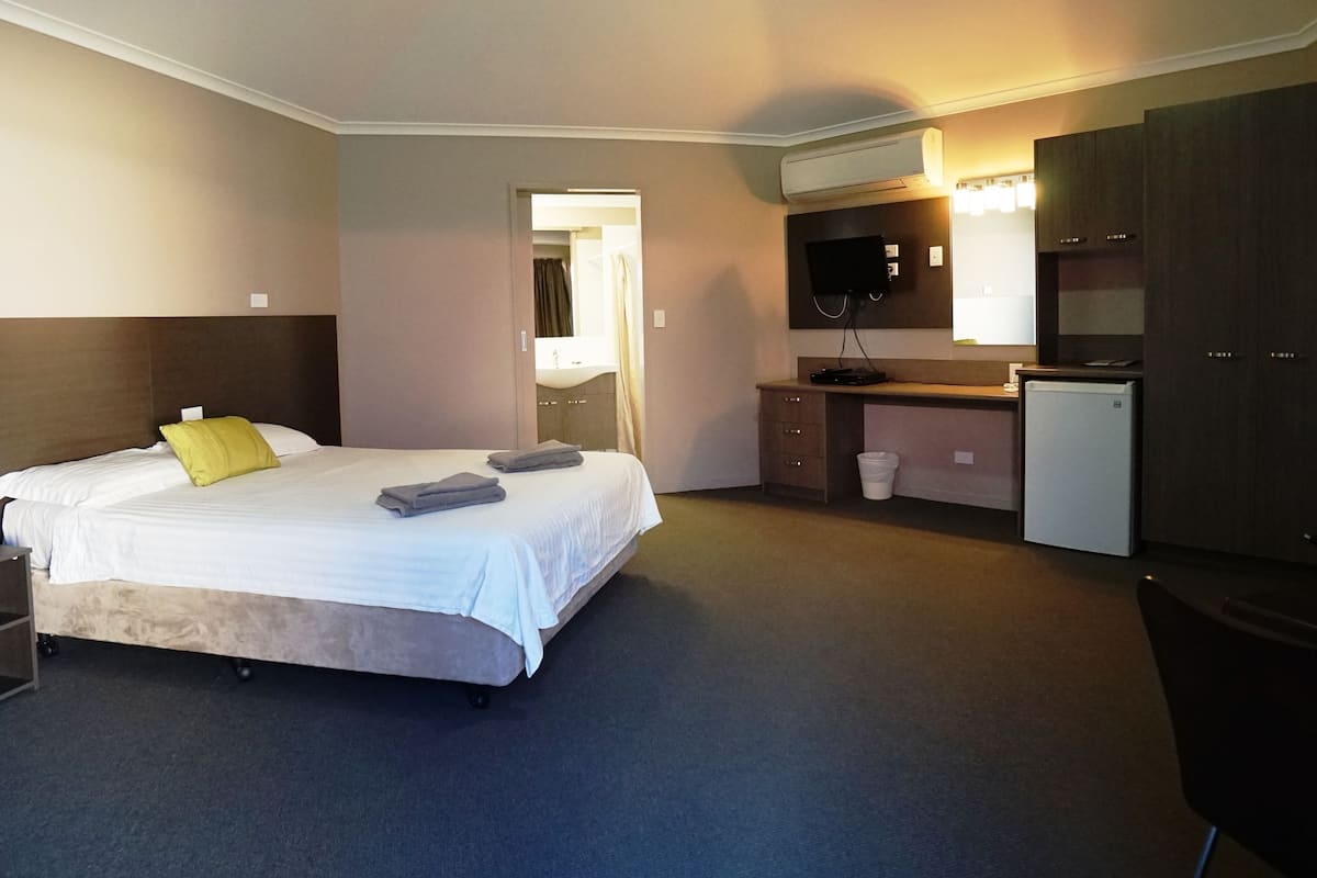A hotel room with a bed, a desk, a mirror, a sink, and a refrigerator.
