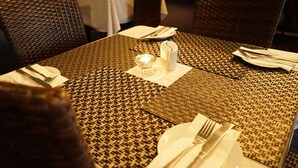Una mesa de comedor lista con platos blancos, cubiertos y una vela.